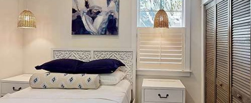 white carved wood bed with a tan, blue, and white embroidered bolster pillow and blue art above the headboard