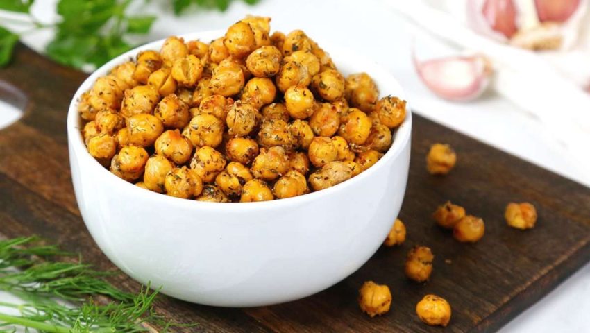 a cutting board with a white bowl full of crispy chickpeas with spices