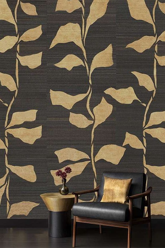 a corner of a room with black leather chair and gold and black side table place in front of black wallpaper with large gold leaves