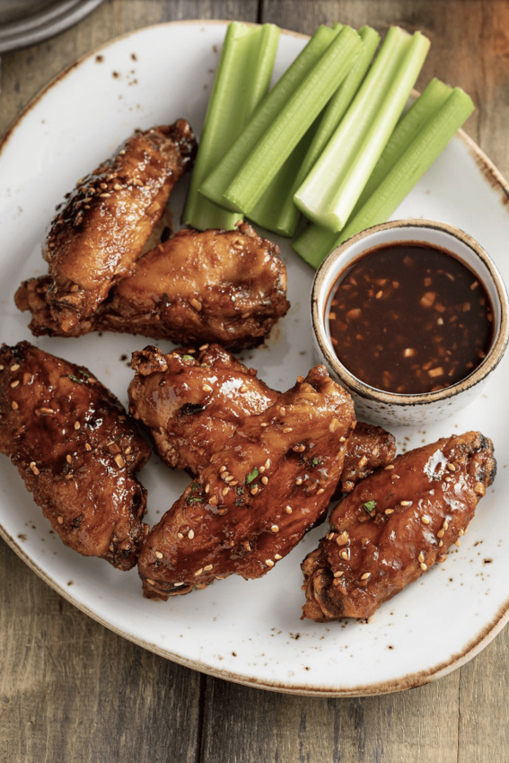 a platter of wings with sesame seed atop with a dipping sauce and celery sticks