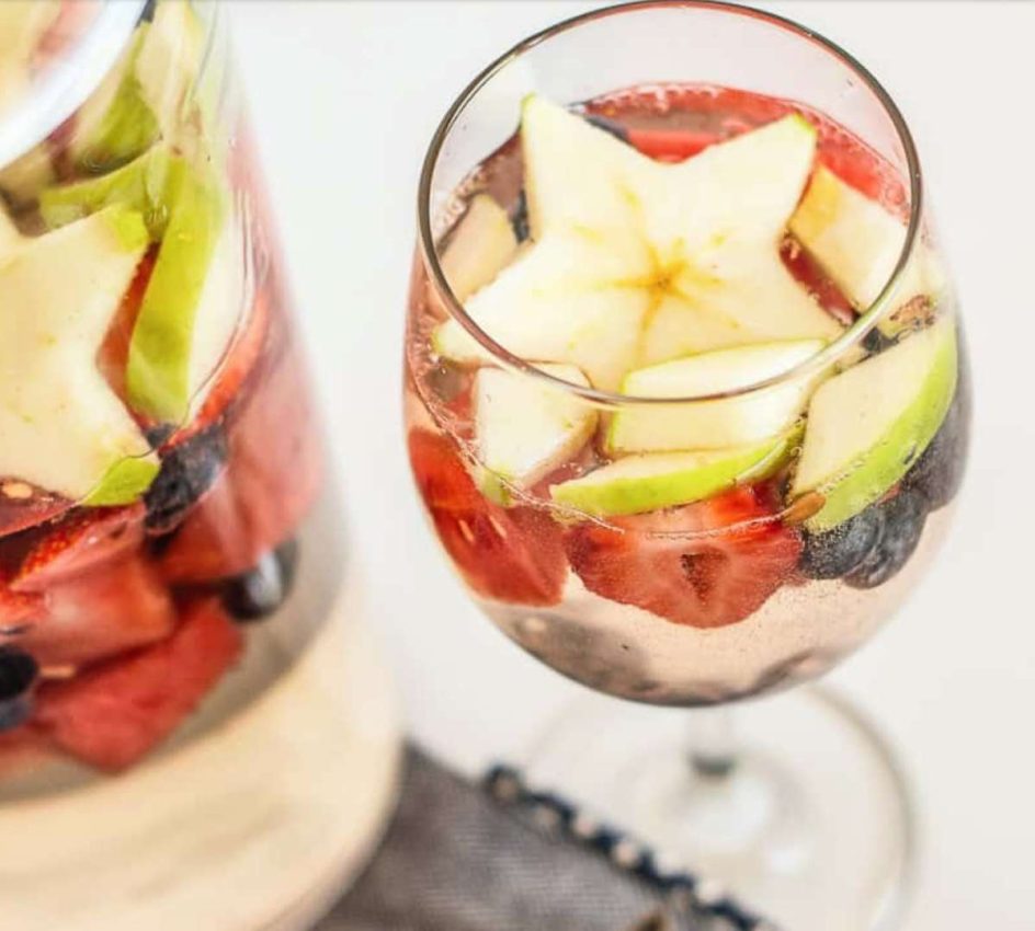 a pitcher and a glass of non-alcoholic white sangria with berries and apples