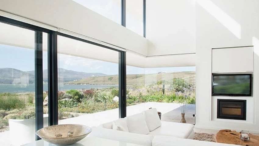 photo of modern home with large windows looking over greenery, mountains, and a lake