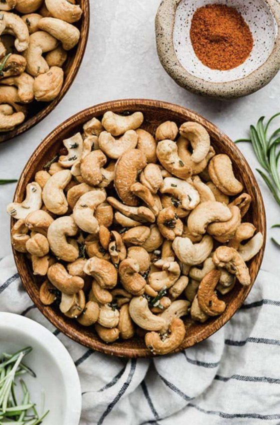 a bowl with roasted cashews and sprigs of rosemary on the table
