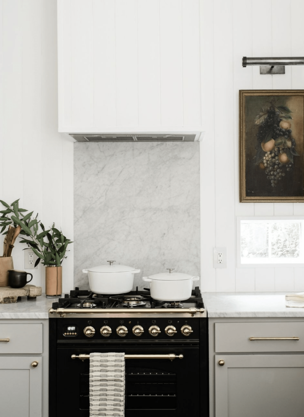 A black range with marble slab backsplash and vertical planks as backsplash behind the cabinetry