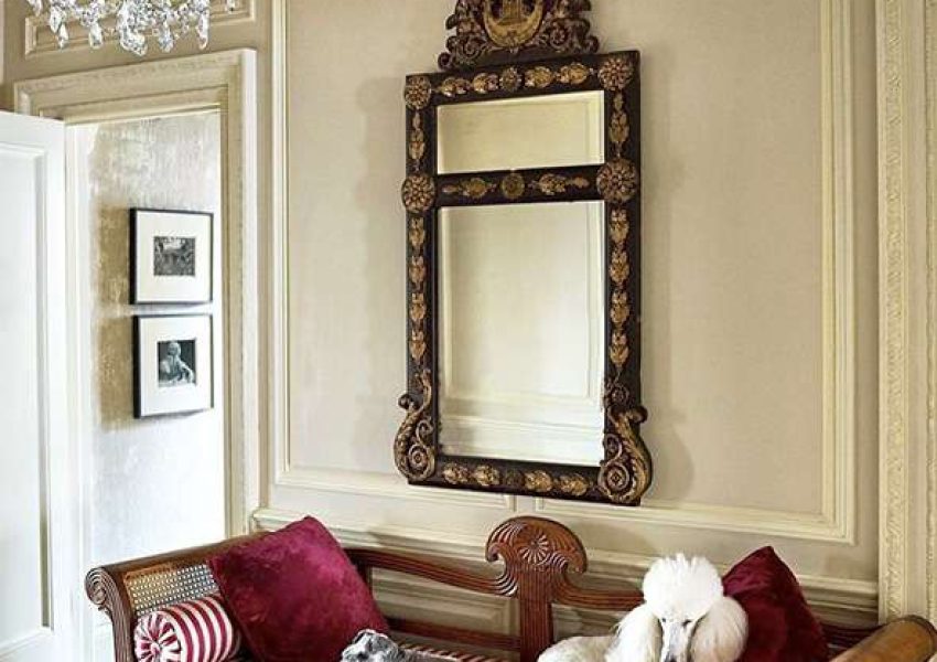 Formal room with thick wainscoting, gold and black mirror, crystal chandelier, cane and fluted wood settee with red and white striped cushion and matching bolsters plus 2 red velvet pillow and 1 coiffed white standard poodle and a miniature schnauzer lounging on the settee