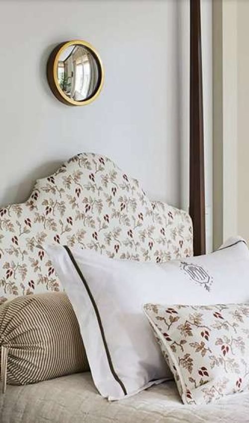 upholstered bed with textured stone-colored coverlet, then layered with bown and white striped bolster tied at the ends, white pillow and sham, lumbar pillow in same fabric as headboard