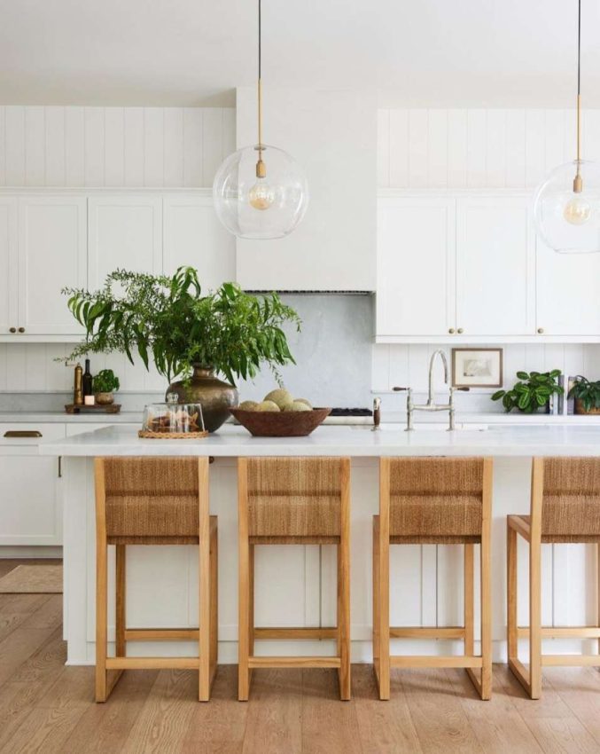 White cabinetry, white vertical plank walls, quartz counters and backsplash, rattan and teack counter stools, west coast styling with woods, matte metals, and greenery