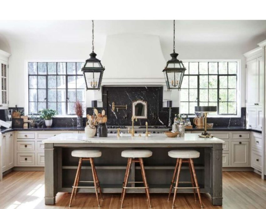 A California-Spanish home with large black-paned windows, wood floors, white cabinetry, black marble counters and backsplash on perimeter, charcoal island with white marble countertop, wood counter stools, 2 large traditional black lanterns over the island, styling with live and dried florals/greenery, wooden accessories, textured pottery