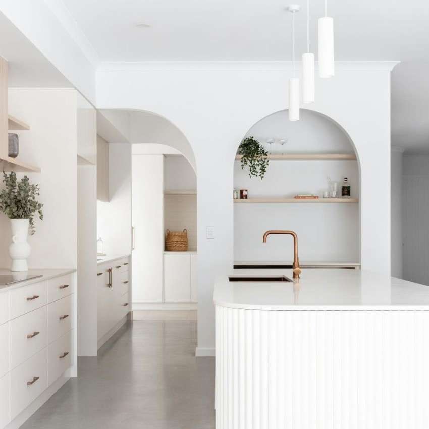 an all-white kitchen - reeded island with sink, white cabinetry, white walls, and white lights